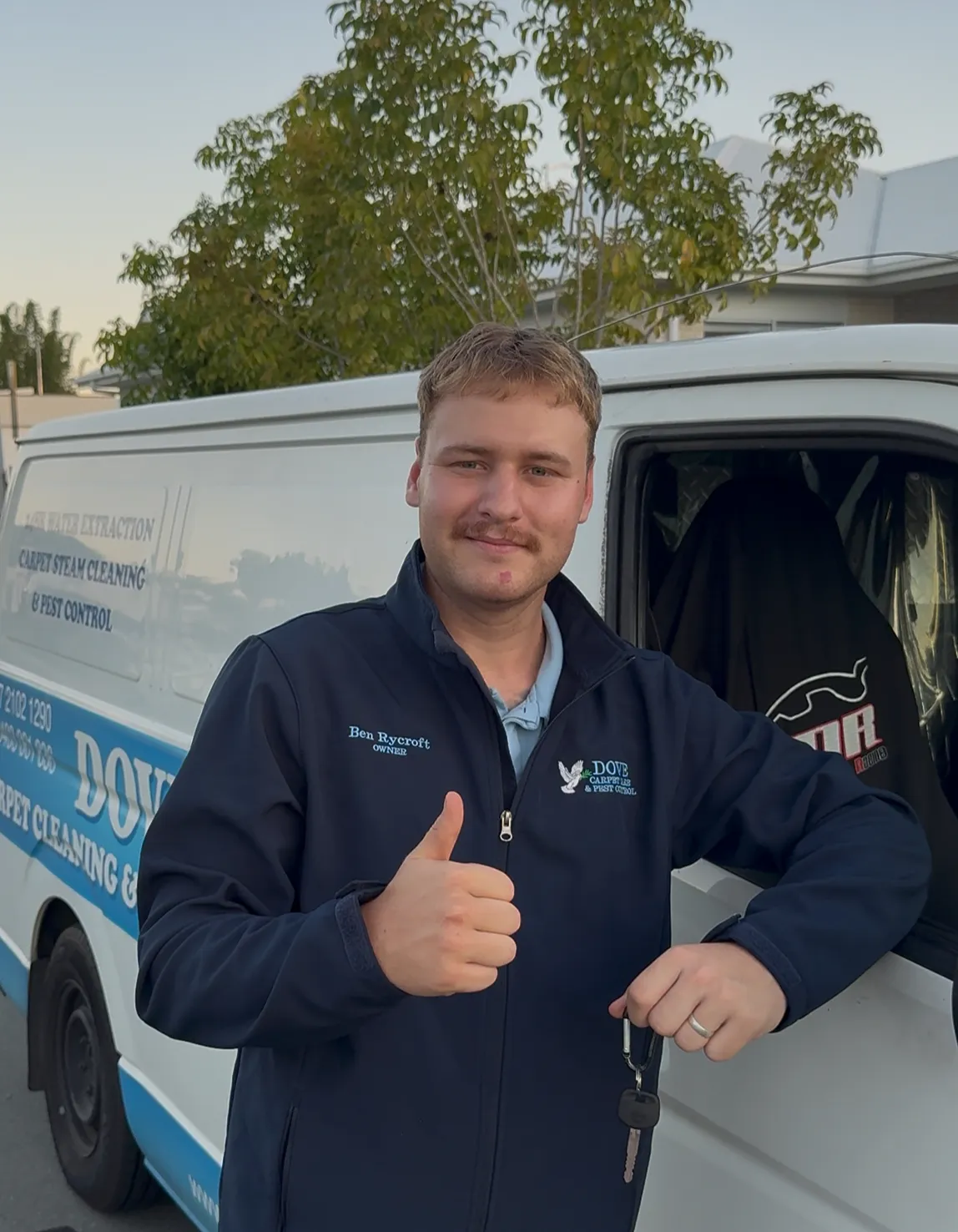 Ben, the carpet cleaner, giving a thumbs up beside his work van at dusk